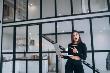 Surprised and happy young woman holding laptop on window background