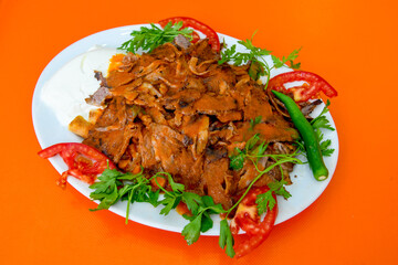 Turkish and Arabic Traditional Ramadan doner kebab with tasty tomato sauce and rice or turkish pilav in white plate on wood table background. ( Pilav ustu doner)