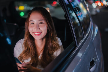 Smiling of asian successful businesswoman use mobile smartphone her sitting back seat in the car after work overtime in modern city at night.