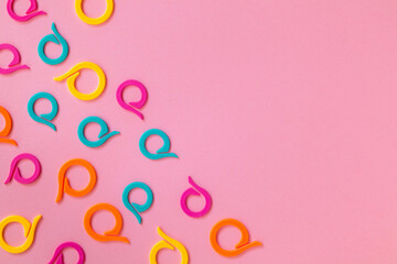 Set of bright colorful plastic knitting markers on a pink background. Top view. Copy space. Handmade concept.