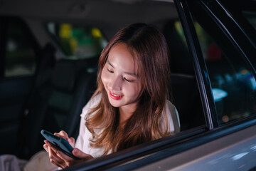 Smiling of asian successful businesswoman use mobile smartphone her sitting back seat in the car after work overtime in modern city at night.