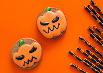 Halloween gingerbread cookies and paper cocktail tubes on an orange background. Halloween party concept. Top view.