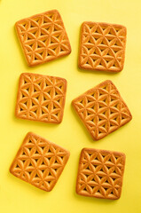 Sweet cookies in a form of square with floral pattern on a yellow background. Top view.