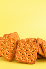 Sweet square shaped biscuits with floral pattern close up on a yellow background. Copy space.
