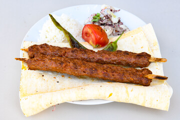 Grilled Turkish Adana, Urfa  Kebab with grilled vegetables, onion and rice on plate. Adana durum .