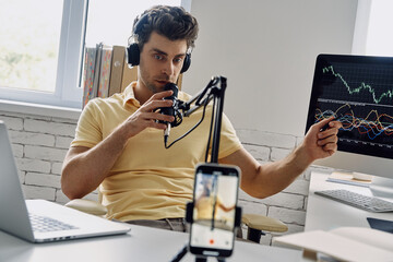 Confident man in headphones using microphone and gesturing while recording his business podcast