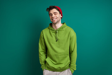 Confident young man looking at camera and smiling while standing against green background