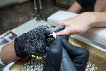 Close-up of a woman in a nail salon getting a manicure in a beauty salon from a beautician who uses an electric nail polish remover machine with flying shards all around.