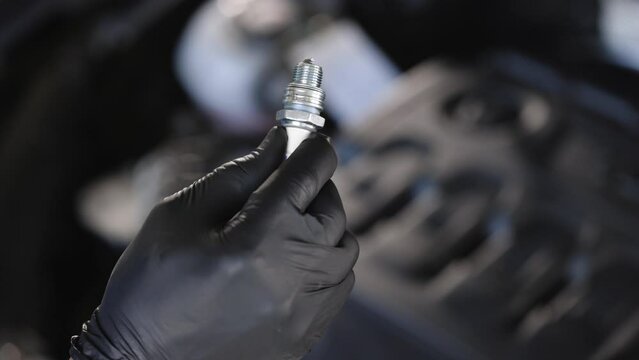 Close up of worker hands changes spark plugs in car engine in auto service. An auto mechanic replaces the spark plugs in the car. Male auto mechanic changes spark plugs in a car engine