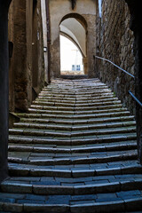 A steep, paved street with the stairs and a stone gate