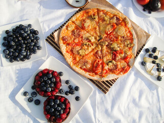 Summer picnic on the beach. food and drink concept. two glasses, wooden tray, Italian pizza, cheese, fruit and a straw hat