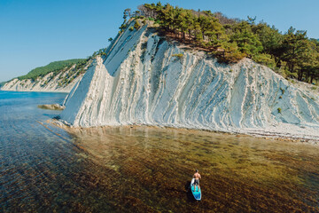 Man traveling on stand up paddle board in sea. Surfer walking on SUP board in sea with scenic...