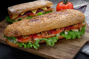 Sandwich with smoked meat, cheese and tomatoes on a wooden board