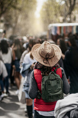 back view of a woman with hat and backpack walking through a traditional market in spain. concept of urban tourism and vacations. vertical format.