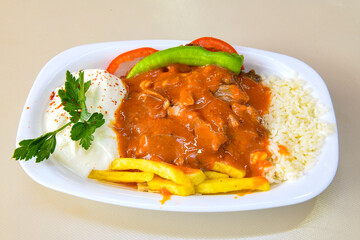 Turkish and Arabic Traditional Ramadan doner kebab with tasty tomato sauce and rice or turkish pilav in white plate on wood table background. ( Pilav ustu doner)
