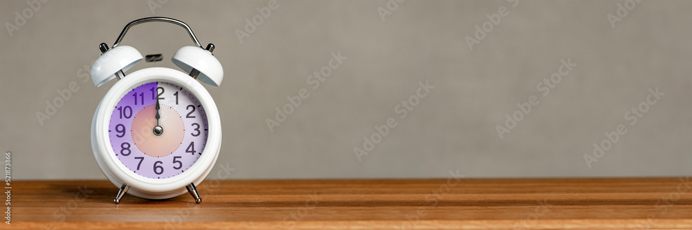 Poster twelve o'clock on the alarm. a white alarm clock stands on a wooden table. the clock hand points to 