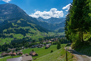 Fototapeta na wymiar Adelboden im Panorama, Bergdorf mit vielen schönen und alten Holzhäusern, Bergwiesen, Wäldern und den hohen Bergen Grosser Lohner und Wildstrubel im Hintergrund. Streusiedlung im Engstligental. 