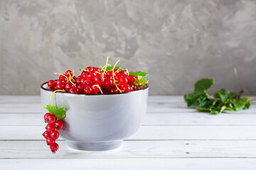 Fresh red currants in a bowl and leaves on the table. Organic summer food.