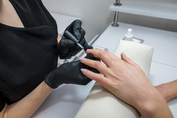 The manicurist applies a base layer to the client's nail.Applying a transparent varnish with a brush.