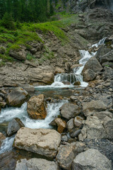 grosser Wasserfall der Engstligen in Adelboden. Das Wasser fett über eine hohe Felswand auf Geröll, Steine und Felsen. Am Ufer hat es Gras, Blumen und Bäume