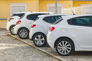 Four similar white hatchback cars parked on street in typical European town