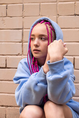 Portrait of a caucasian teenage hipster girl with pink braids using an earphones against a pink brick wall.Summer and technology concept.Generation Z style.