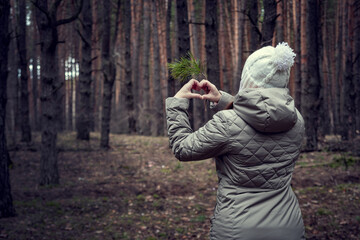 A man in light clothes shows a heart with his fingers, in a coniferous forest. The girl shows her love for nature and the forest.