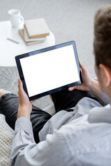 Virtual life. Casual man. Computer mockup. Relaxed unrecognizable guy sitting home with tablet computer with blank screen in light room interior.