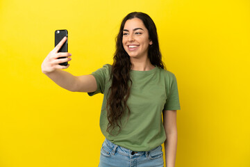 Young caucasian woman isolated on yellow background making a selfie