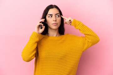 Young caucasian woman using mobile phone isolated on pink background having doubts and thinking