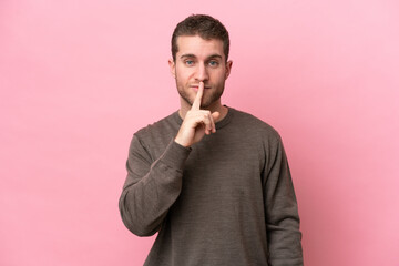 Young caucasian man isolated on pink background showing a sign of silence gesture putting finger in mouth