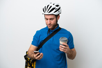 Young caucasian man with thermal backpack isolated on white background holding coffee to take away and a mobile