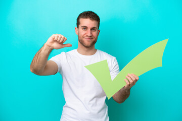 Young caucasian man isolated on blue background holding a check icon with proud gesture