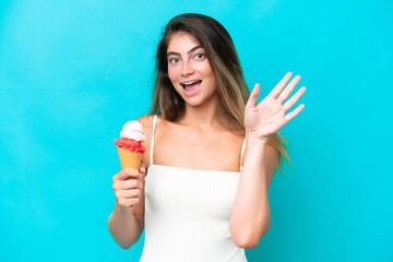 Young woman in swimsuit holding an ice cream isolated on blue background saluting with hand with happy expression
