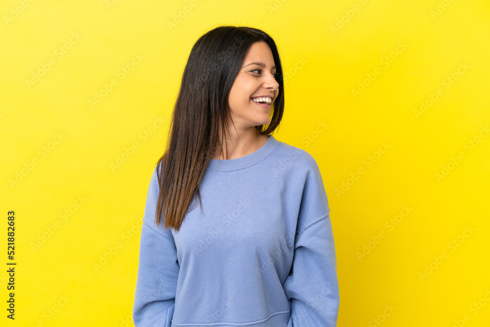 Wall mural Young caucasian woman isolated on yellow background looking to the side and smiling