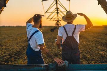 Farmers standing in field looking surveying. Two men next to center pivot irrigation system modern...