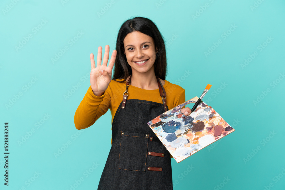 Wall mural Young artist caucasian woman holding a palette isolated on blue background happy and counting four with fingers