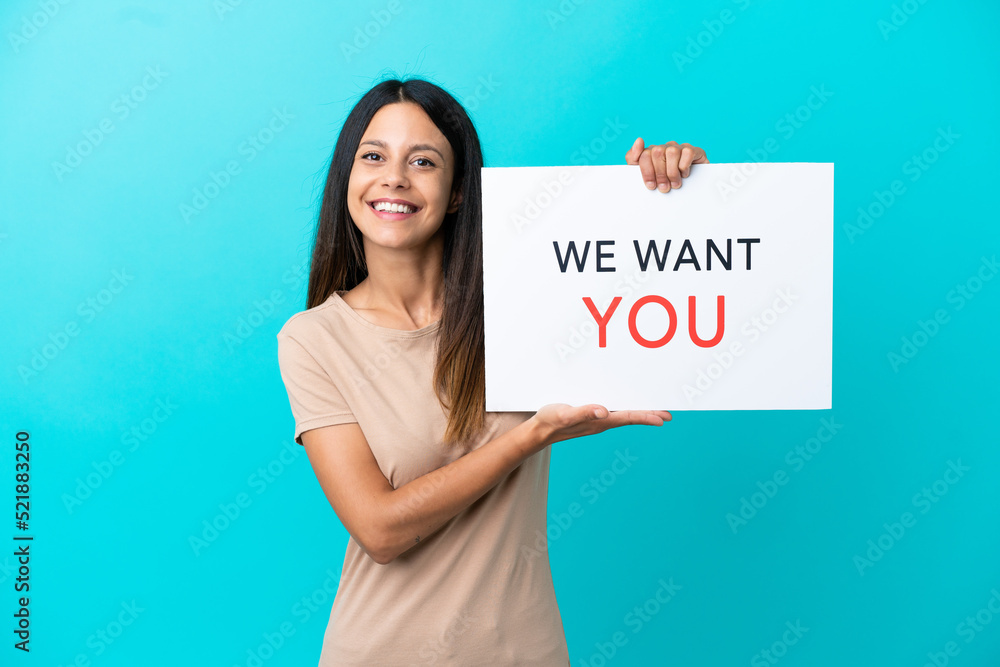 Wall mural Young woman over isolated background holding We Want You board with happy expression