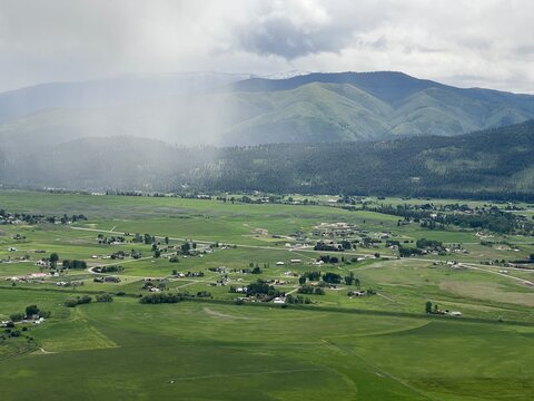 Aerial View Of Lush, Green Farmland, Fields, Homes, Hills And Mountains In Missoula Area, Montana, USA. Rain Clouds Overhead