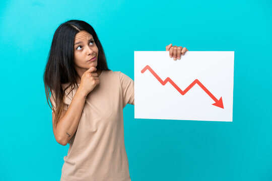 Young woman over isolated background holding a sign with a decreasing statistics arrow symbol and thinking