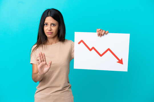 Young woman over isolated background holding a sign with a decreasing statistics arrow symbol and doing stop sign