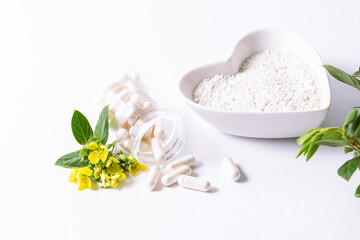 Obraz na płótnie Canvas Different types of collagen, capsules and powder on white background with fresh green leaves and flowers.