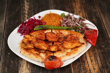 Grilled Turkish chicken wings served with pita, garnish,  onions, bulgur, roasted green pepper, and roasted tomato on white plate on wooden background. Served special restaurant presentation