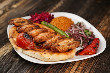 Grilled Turkish chicken wings served with pita, garnish,  onions, bulgur, roasted green pepper, and roasted tomato on a white plate on wooden background. Served special restaurant presentation