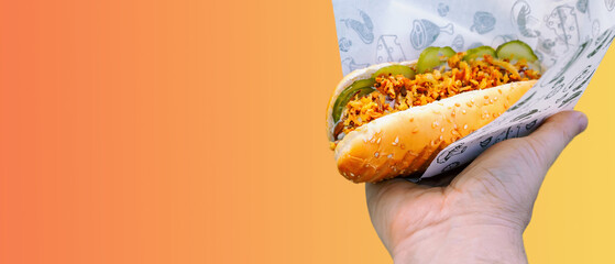 man holds hot dog in his hand on colored background, popular fast food, casual street food, for...