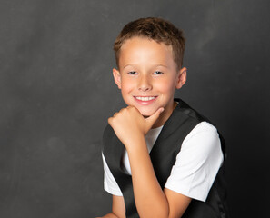 Smiling confident boy in black vest and white t shirt hand on chin - 521885243
