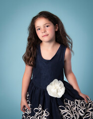 Young girl with long brown hair in embroidered blue party dress with white flower - 521885296