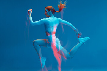 Running workout. Athlete woman runs in air on blue studio backdrop. Long exposure. Motion blur....
