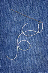Sewing thread and needle at jeans denim background. Tailor texture handmade jeans concept