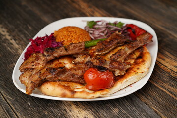 Grilled lamb chops on a white plate on wooden background. Grilled lamb with pita, garnish,  onions, bulgur, roasted green pepper, and roasted tomato. Turkish name: kuzu pirzola. 